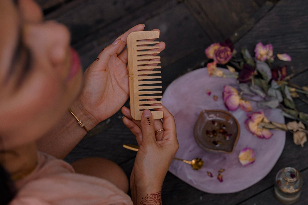 Hands holding a wooden comb above a ritual plate of dried roses